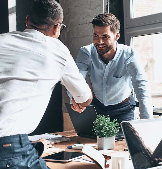 Smiling colleagues shake hands, laptops on table